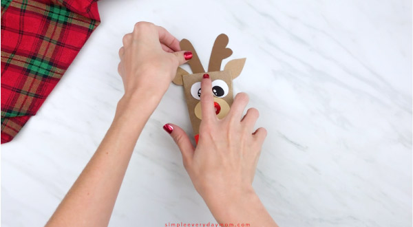 hands gluing antlers onto toilet paper roll reindeer craft
