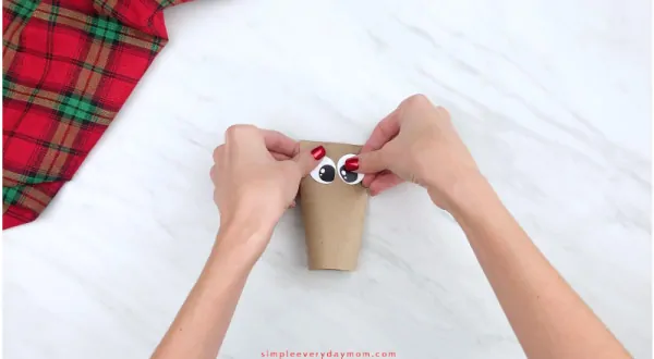 hands gluing eyes onto toilet paper roll reindeer craft