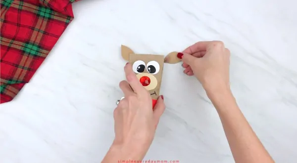 hands gluing ears onto toilet paper roll reindeer craft