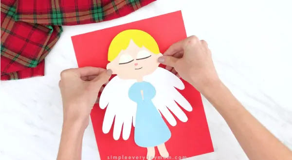 Hands gluing handprint angel to red paper 