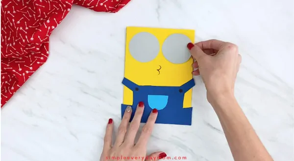 Hands gluing minion goggles onto card 