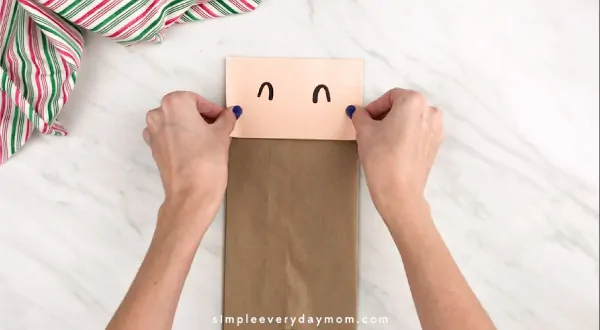 Hands gluing Santa face on paper bag
