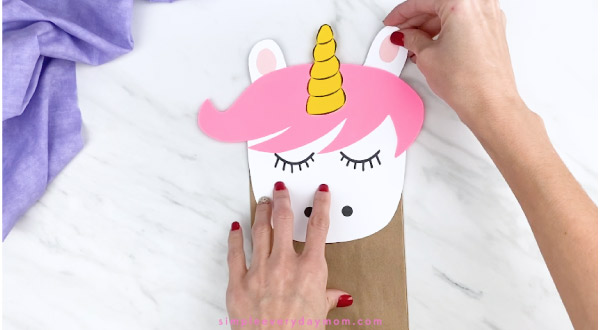 hands gluing ears to back of unicorn paper bag craft