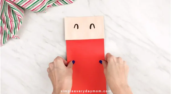 Hands gluing red paper to paper bag Santa 