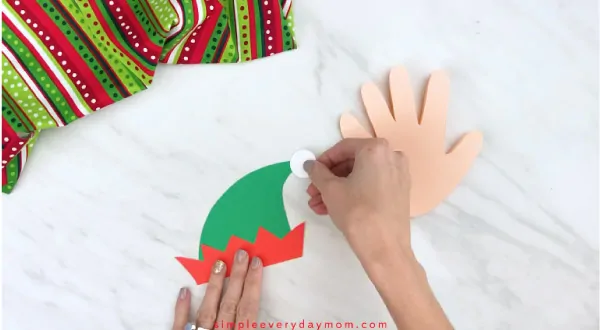 Hands gluing white puff onto elf hat craft 