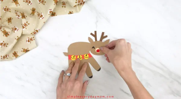 Hands gluing head onto handprint reindeer body 
