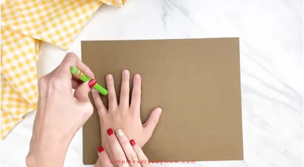adult hands tracing childs hand on brown paper