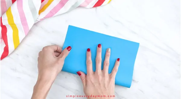 Hands folding piece of blue paper in half 