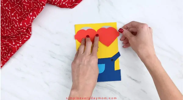Hands gluing heart sunglasses onto minion card 