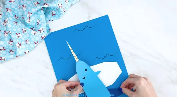 Hands gluing narwhale to blue paper 
