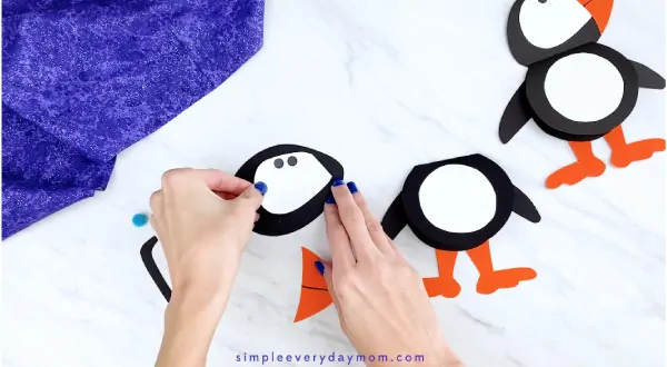 Hands gluing puffin face to head 
