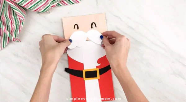Hands gluing Santa mustache to face 