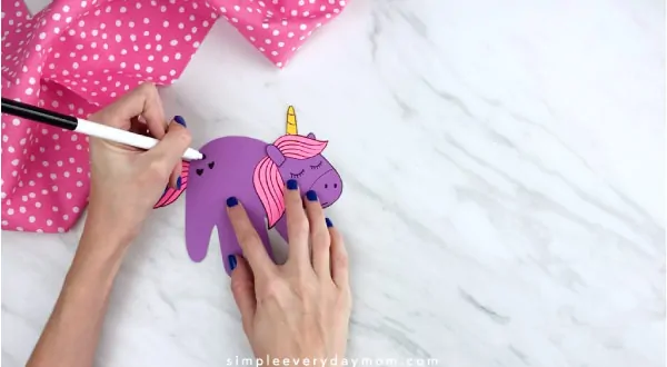 Hands drawing hearts onto handprint unicorn 