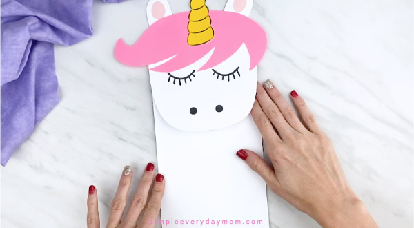 hands gluing body onto unicorn paper bag puppet