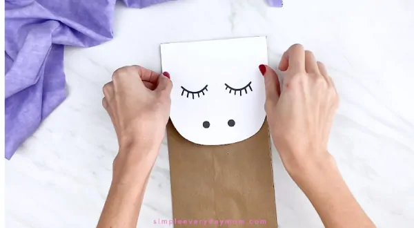 hands gluing unicorn face onto brown paper bag