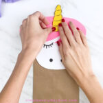 hands gluing unicorn horn onto paper bag unicorn
