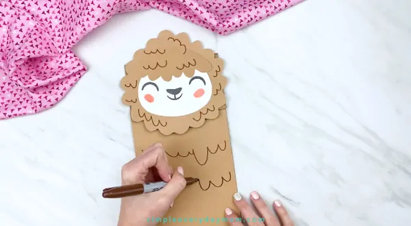 hands drawing on llama fluff onto paper bag craft