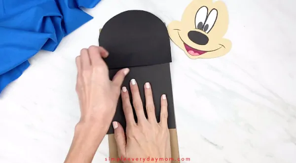 hands gluing mickey mouse body onto paper bag