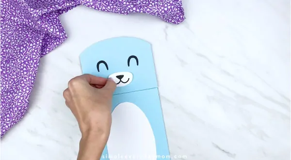 Hands gluing nose and mouth to paper bag bunny craft 