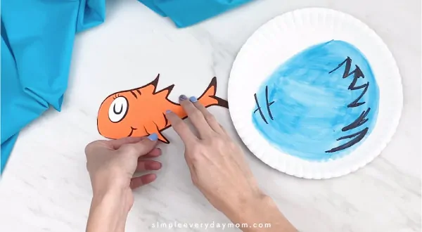 Hands gluing fish fin onto Dr. Seuss craft 