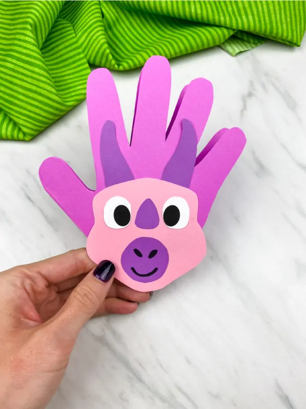 hand holding pink and purple handprint dinosaur card 