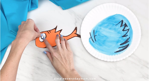 Hands gluing eyes onto Dr. Seuss fish 