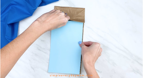 Hand gluing blue paper to brown paper bag 