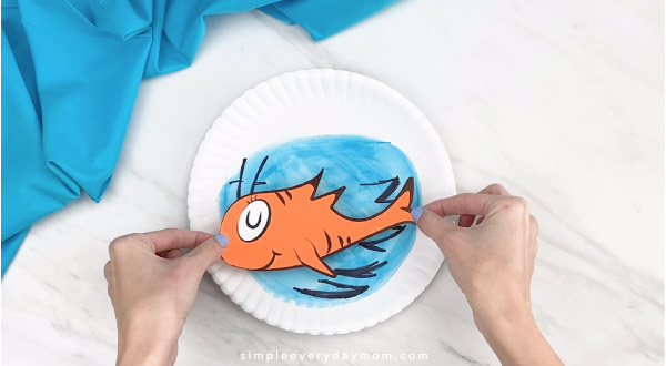 Hands gluing Dr. Seuss fish onto paper plate craft 