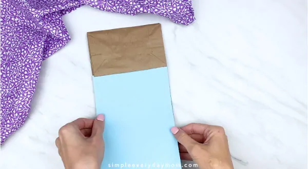 Hands gluing blue paper onto brown paper bag 