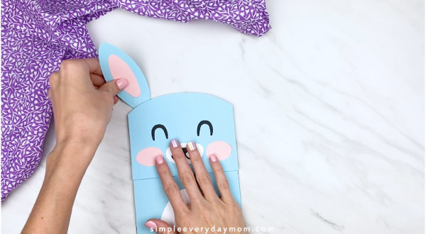 Hands gluing ears to paper bag bunny craft 