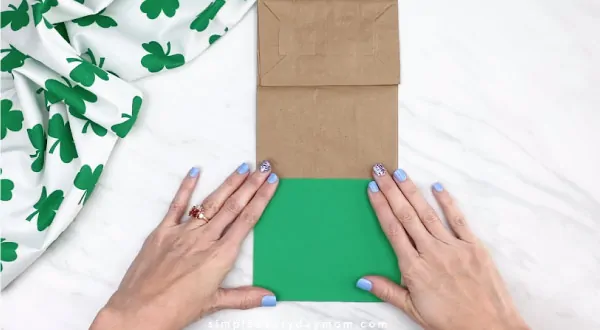 Hands gluing green paper onto brown paper bag 