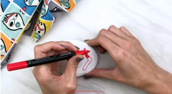 hands coloring in Forky\'s eyebrow with red paint pen 