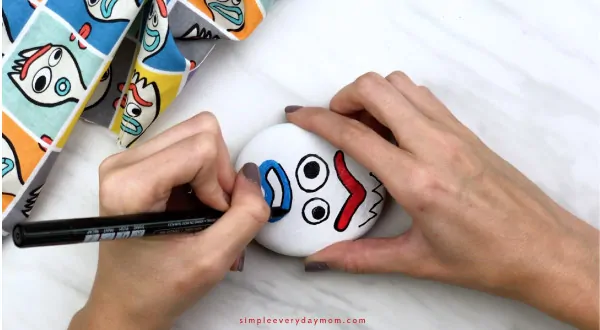 hands outlining Forky\'s mouth with black paint pen 