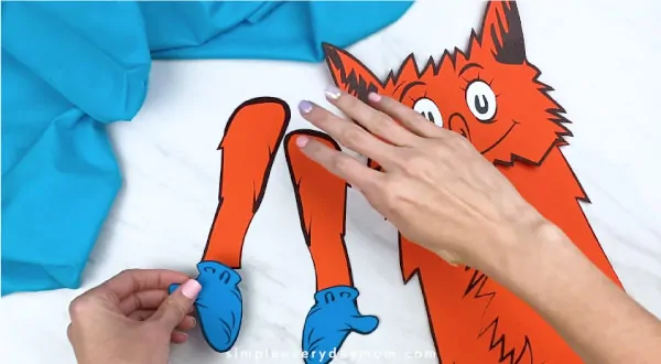 Hands gluing fox in socks mittens to arms 