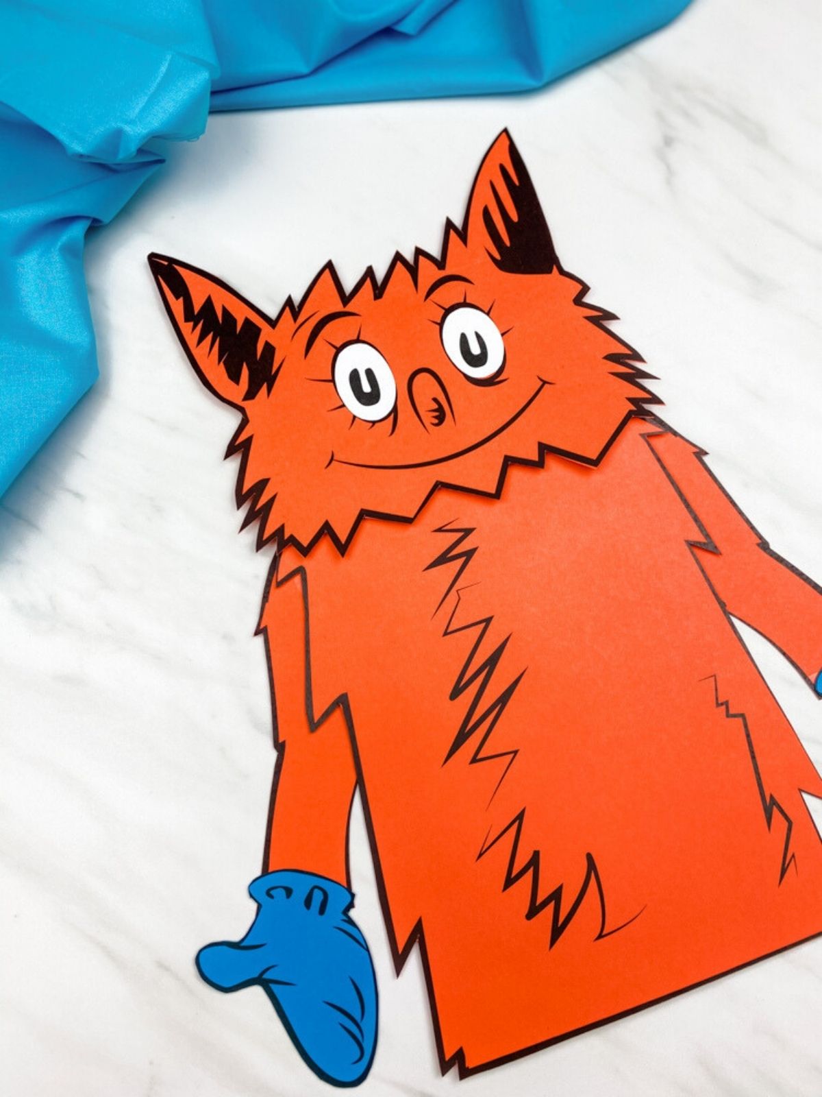 Close-up of the completed orange fox puppet showing its face, pointed ears, and blue mittens.