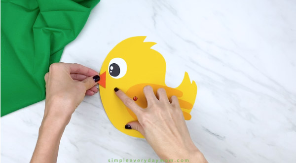 Hands gluing beak onto handprint chick craft 