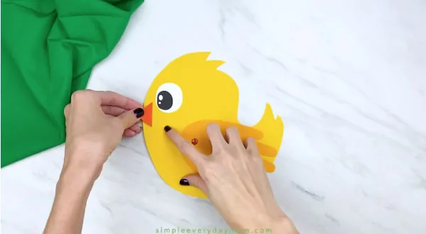 Hands gluing beak onto handprint chick craft 