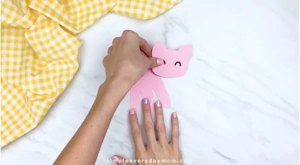 Hands gluing pig head onto handprint pig craft 