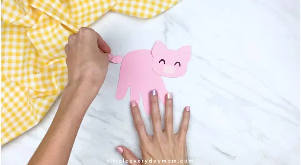 Hands gluing tail onto handprint pig craft 