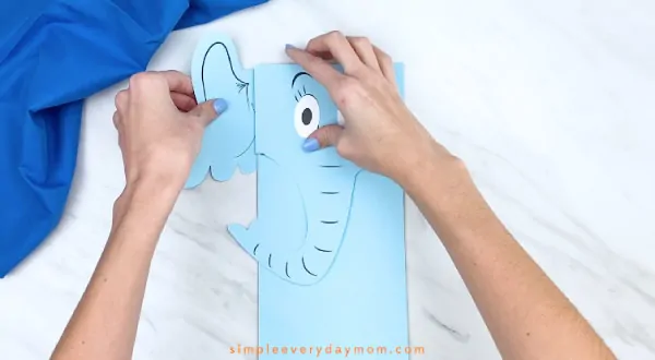 Hands gluing ears to back of Horton paper bag craft 