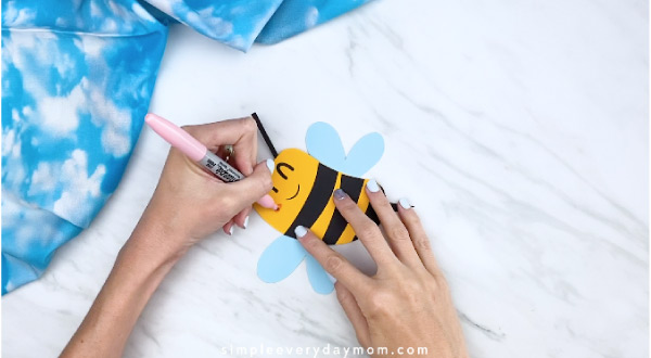 Hands drawing cheeks onto paper bee card