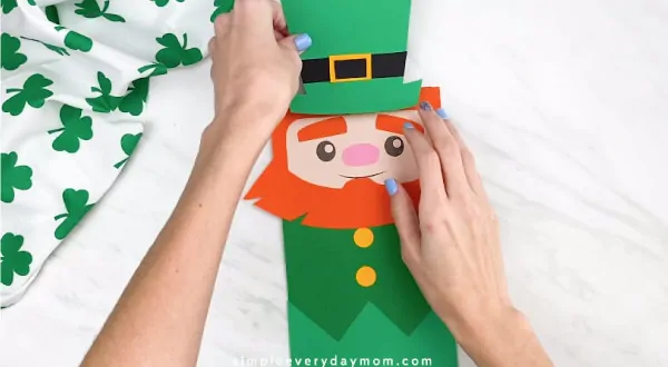 Hands gluing leprechaun hat onto paper bag leprechaun craft 