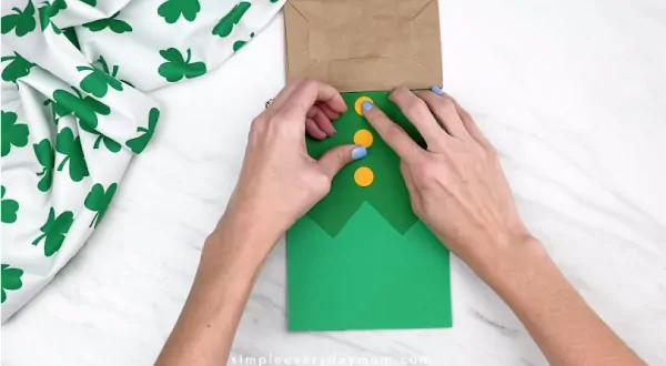 Hands gluing buttons onto paper bag leprechaun 