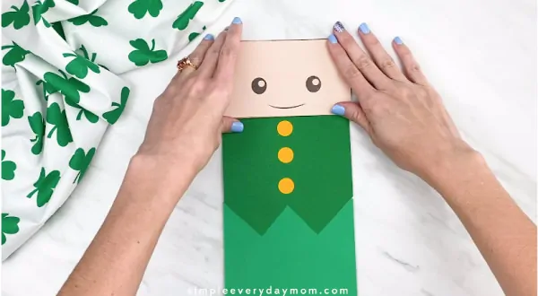 Hands gluing leprechaun face onto paper bag 