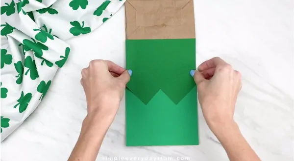 Hands gluing green vest onto paper bag 