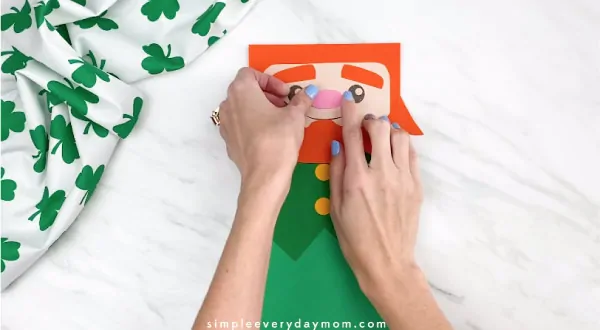 Hands gluing nose onto paper bag leprechaun craft 