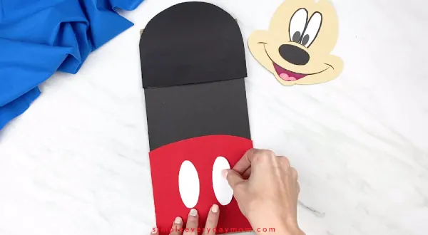 hands gluing buttons onto mickey mouse pants