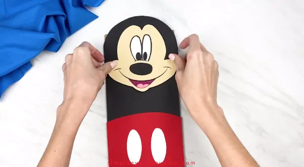 hands gluing mickey mouse face onto paper bag craft