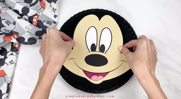 hands gluing mickey face onto black paper plate