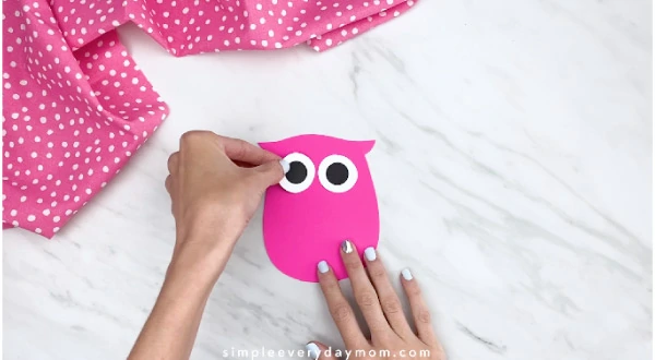 hands gluing on eyes to pink paper owl 